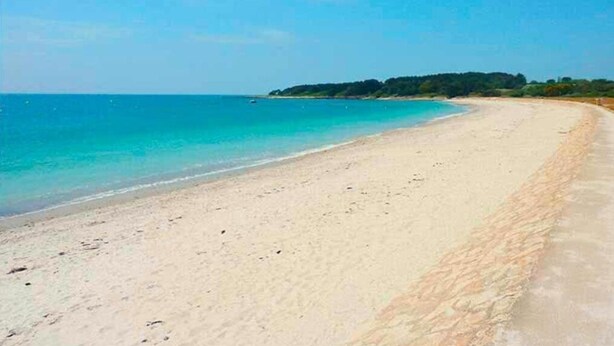 A wide sandy beach with clear turquoise water and a forested island in the distance.