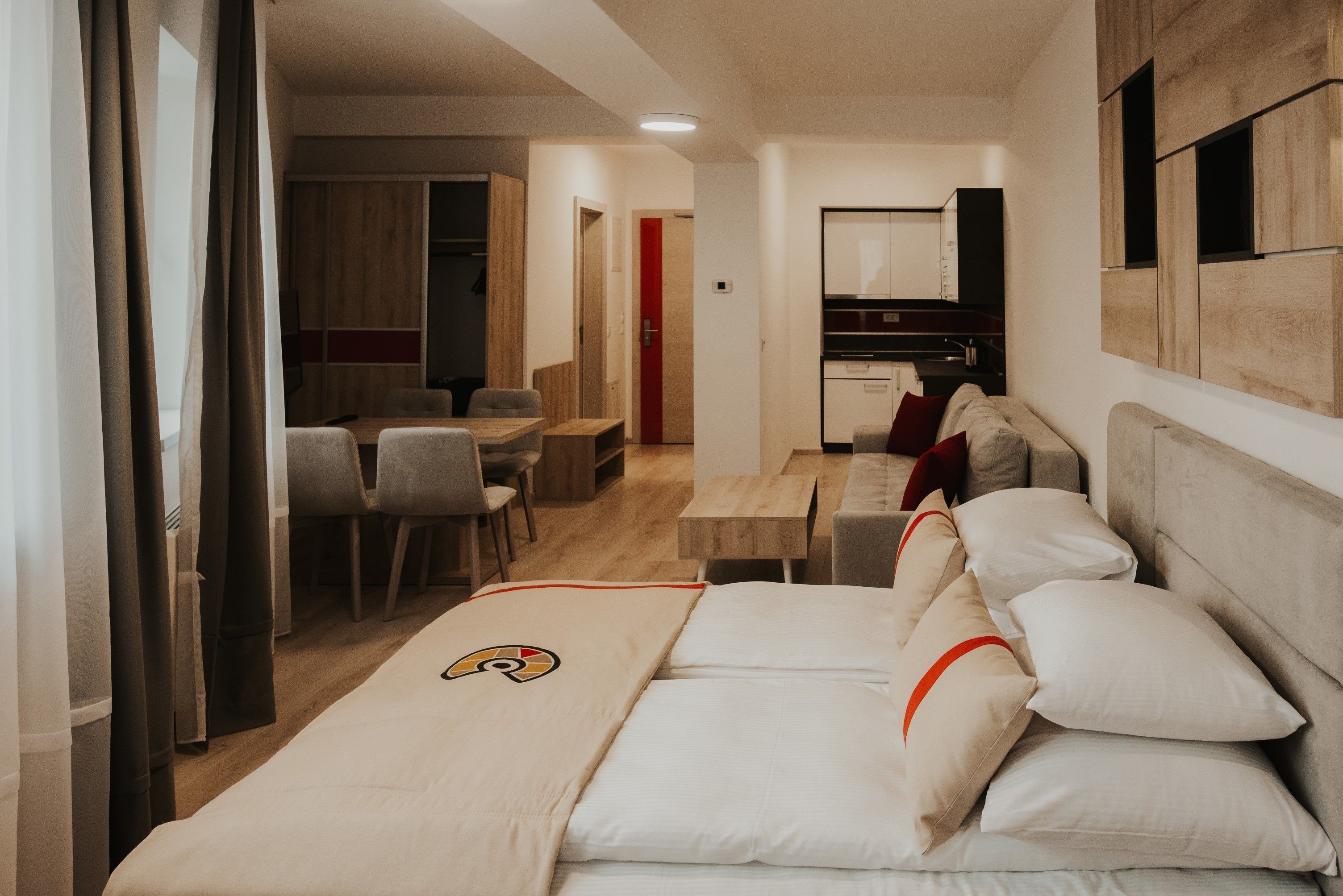 A modern hotel room with a large bed, a desk, and a kitchenette.