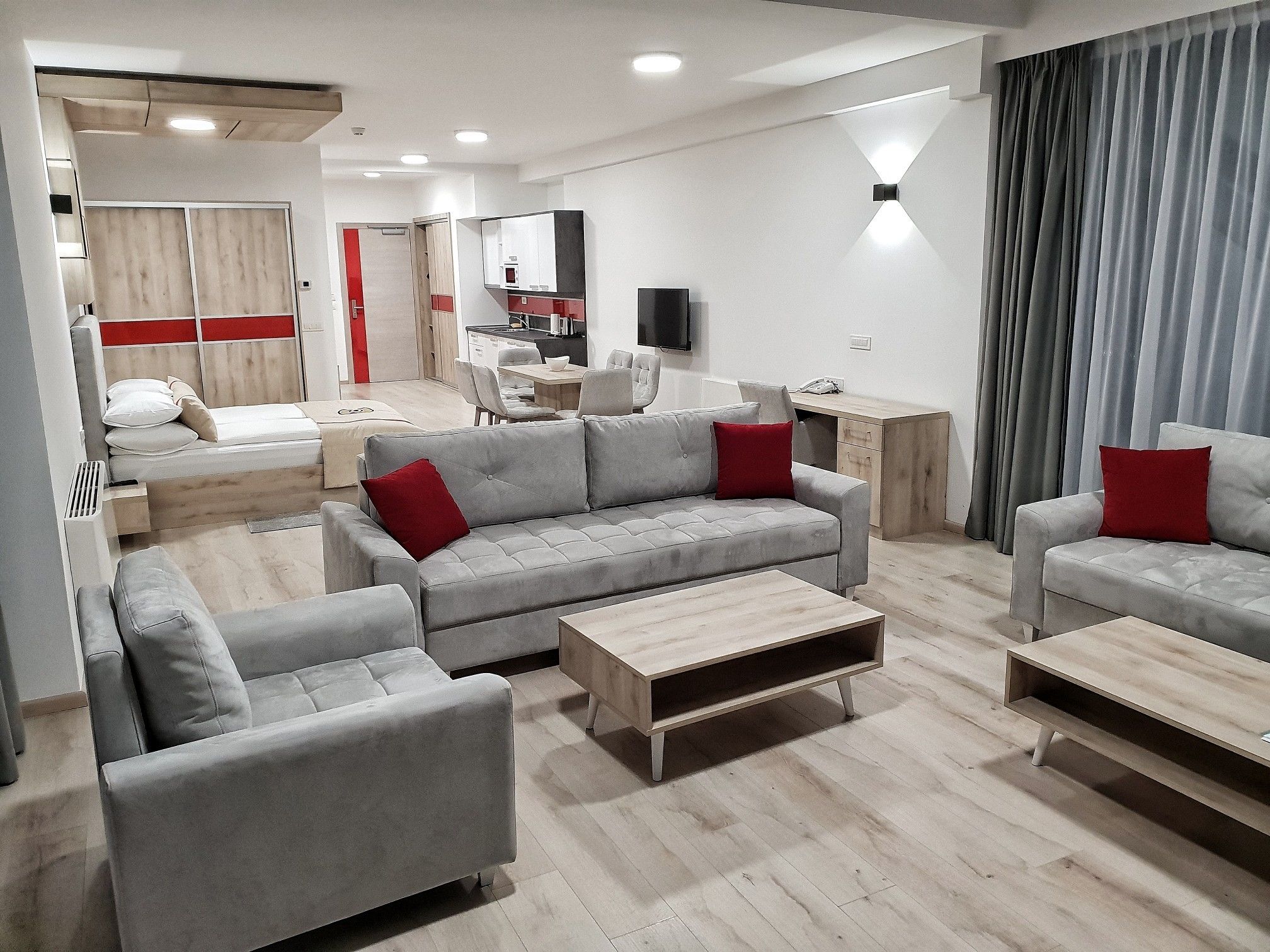 Een moderne woonkamer met grijze banken, een houten salontafel en een eetgedeelte met een rode accentmuur.