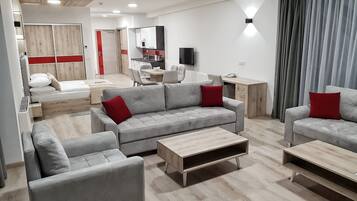 Een moderne woonkamer met grijze banken, een houten salontafel en een eetgedeelte met een rode accentmuur.