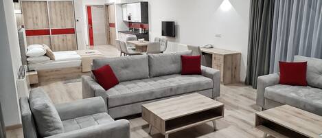 A modern living room with grey sofas, a wooden coffee table, and a dining area with a red accent wall.