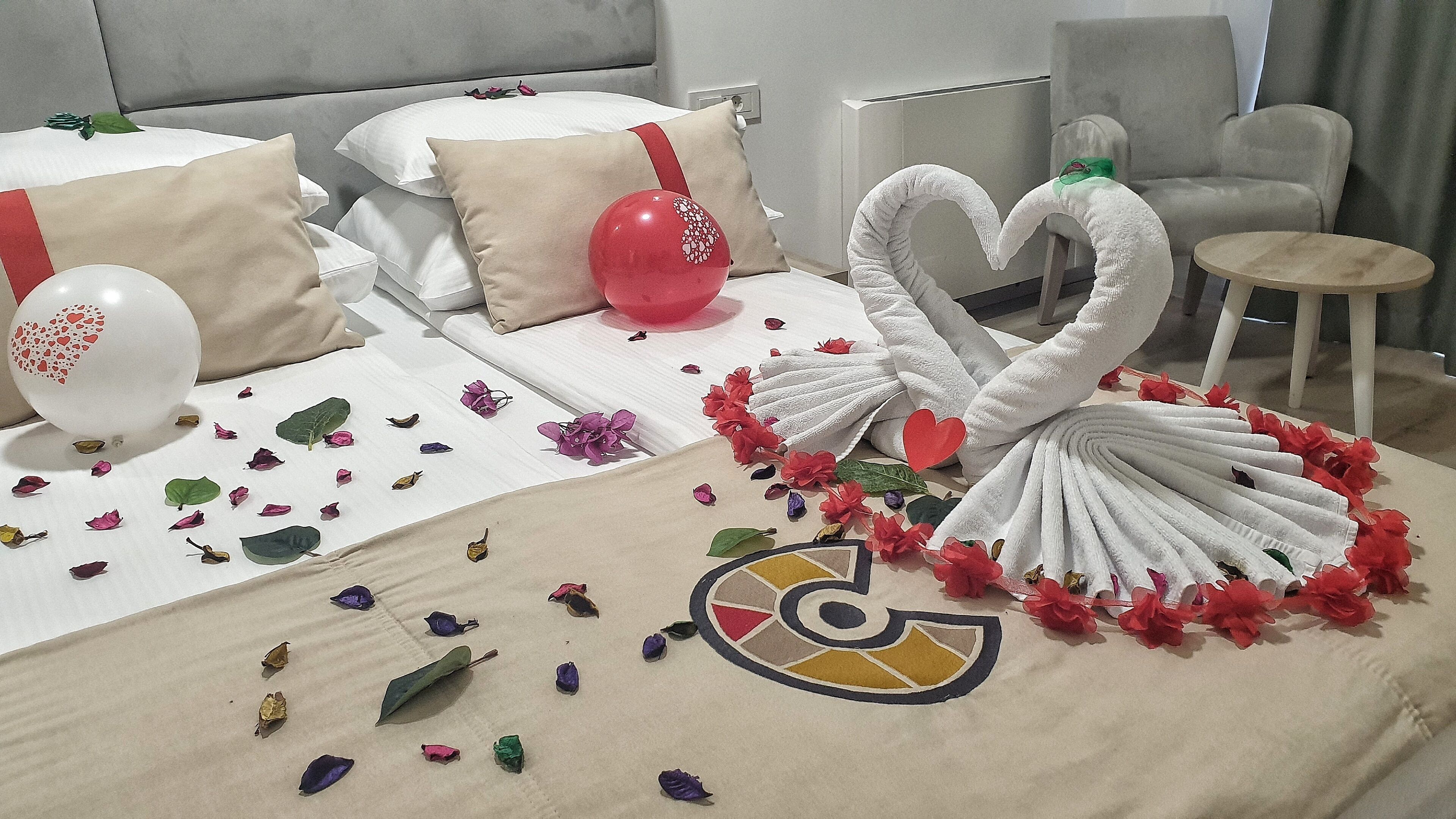 Een net opgemaakt bed met witte lakens, een rode ballon en decoratieve zwanen van handdoeken.