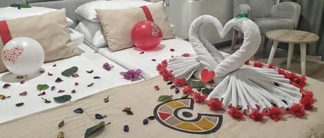 A neatly made bed with white linens, a red balloon, and decorative swans made of towels.