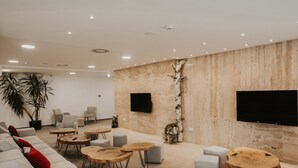 A modern lounge area with a sofa, round wooden tables, and a flat-screen TV mounted on the wall. - Aparthotel Centar Sarajevo (Sarajevo)