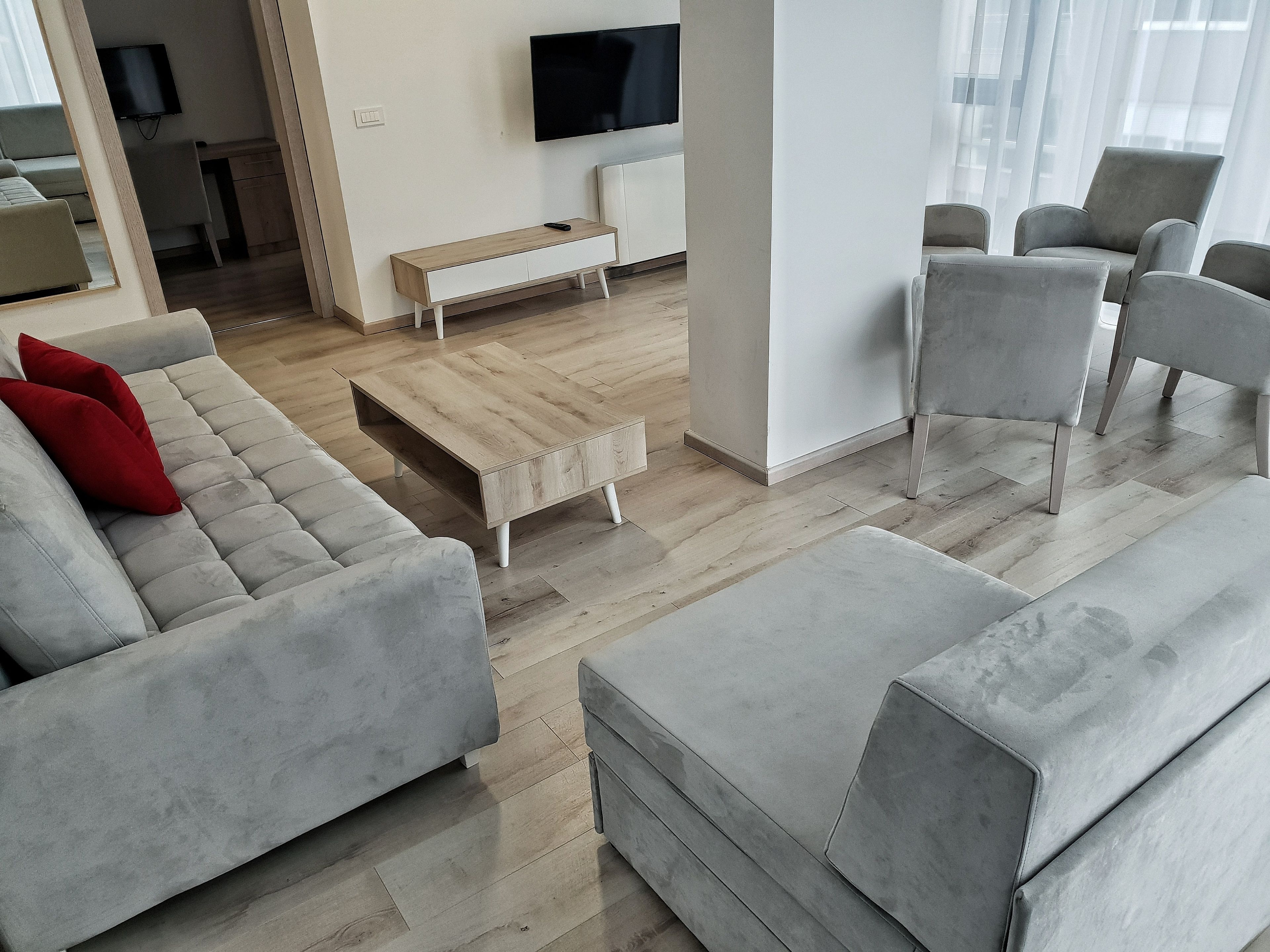 A modern living room with grey sofas, a wooden coffee table, and a TV mounted on the wall.