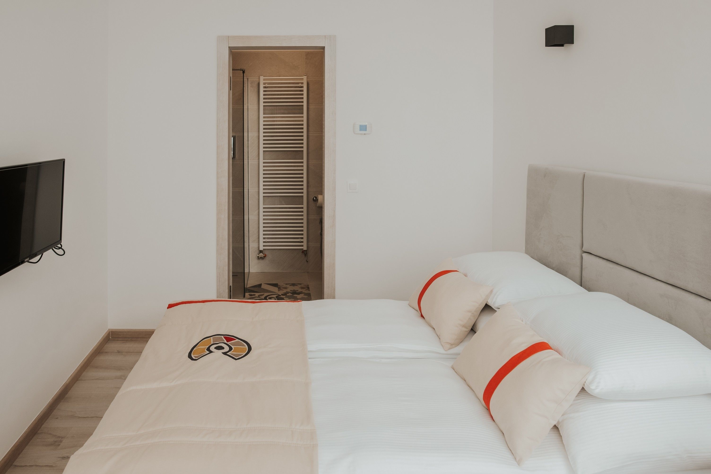 A bedroom with a bed, a TV mounted on the wall, and a door leading to a bathroom.