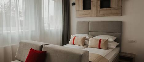 Une chambre d’hôtel moderne, équipée d’un lit, d’un canapé et d’une grande fenêtre avec des rideaux légers.
