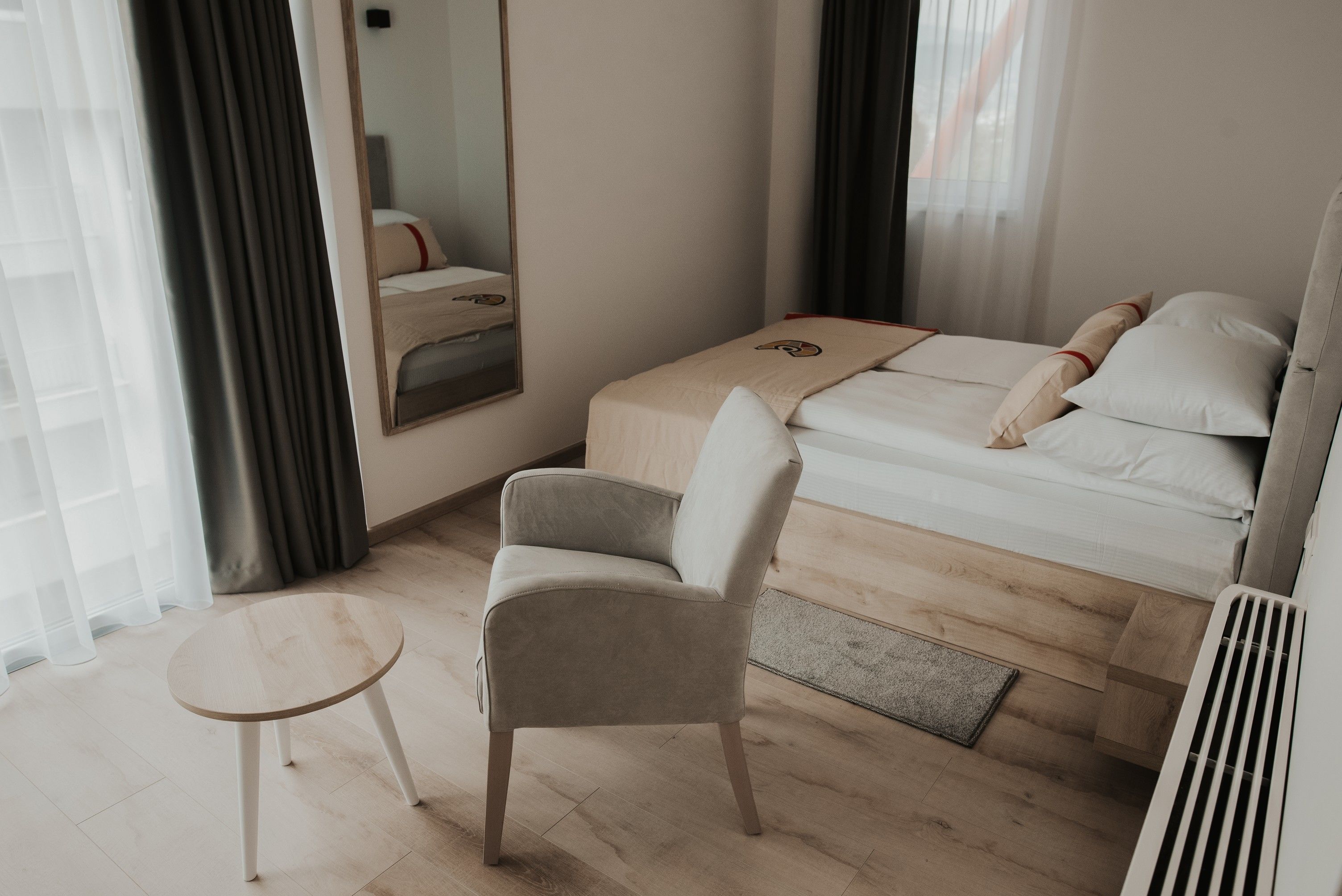 A hotel room with a bed, a chair, a small table, and a mirror.