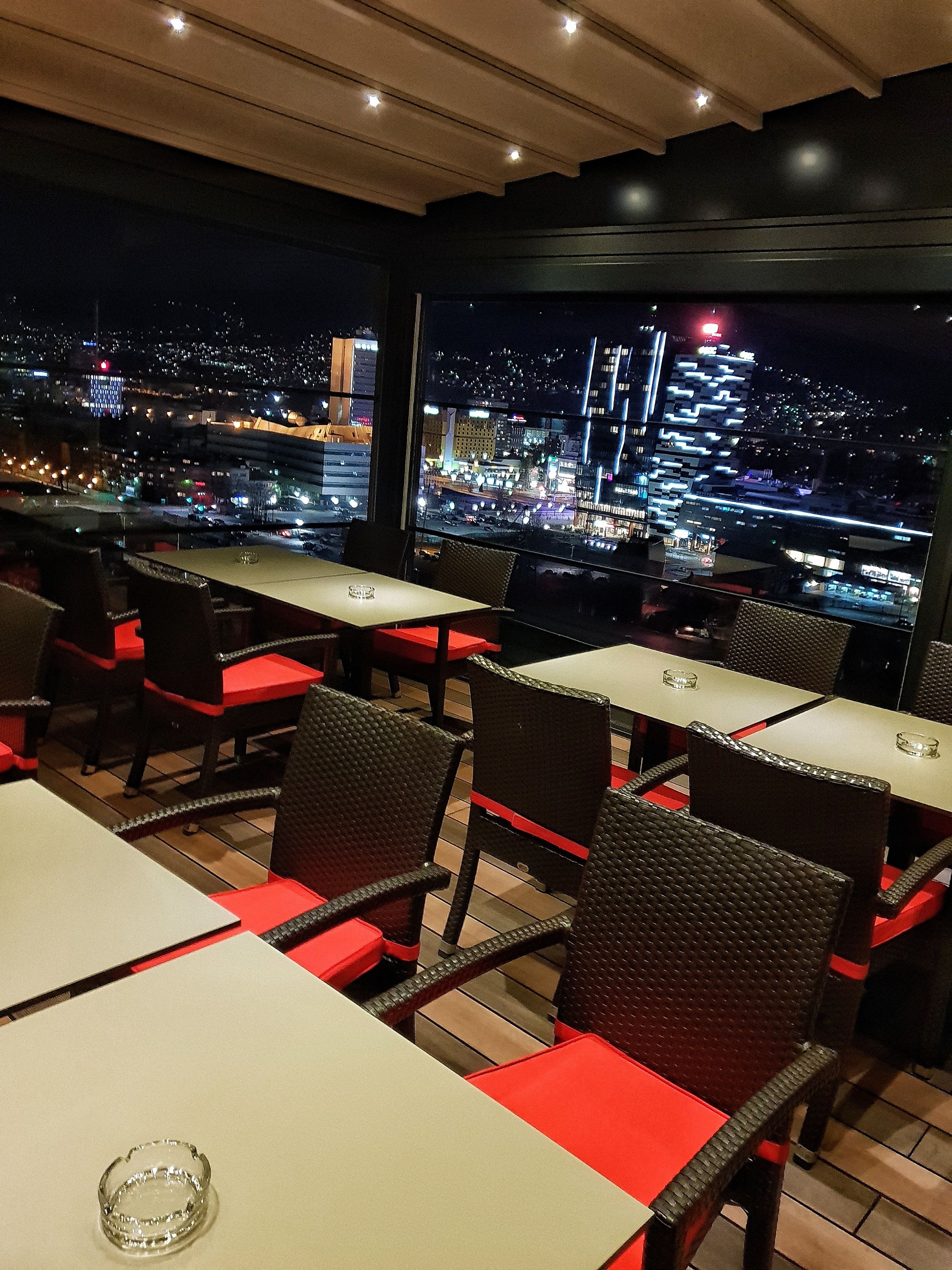Un restaurant avec des tables et des chaises, offrant une vue sur le paysage urbain la nuit.