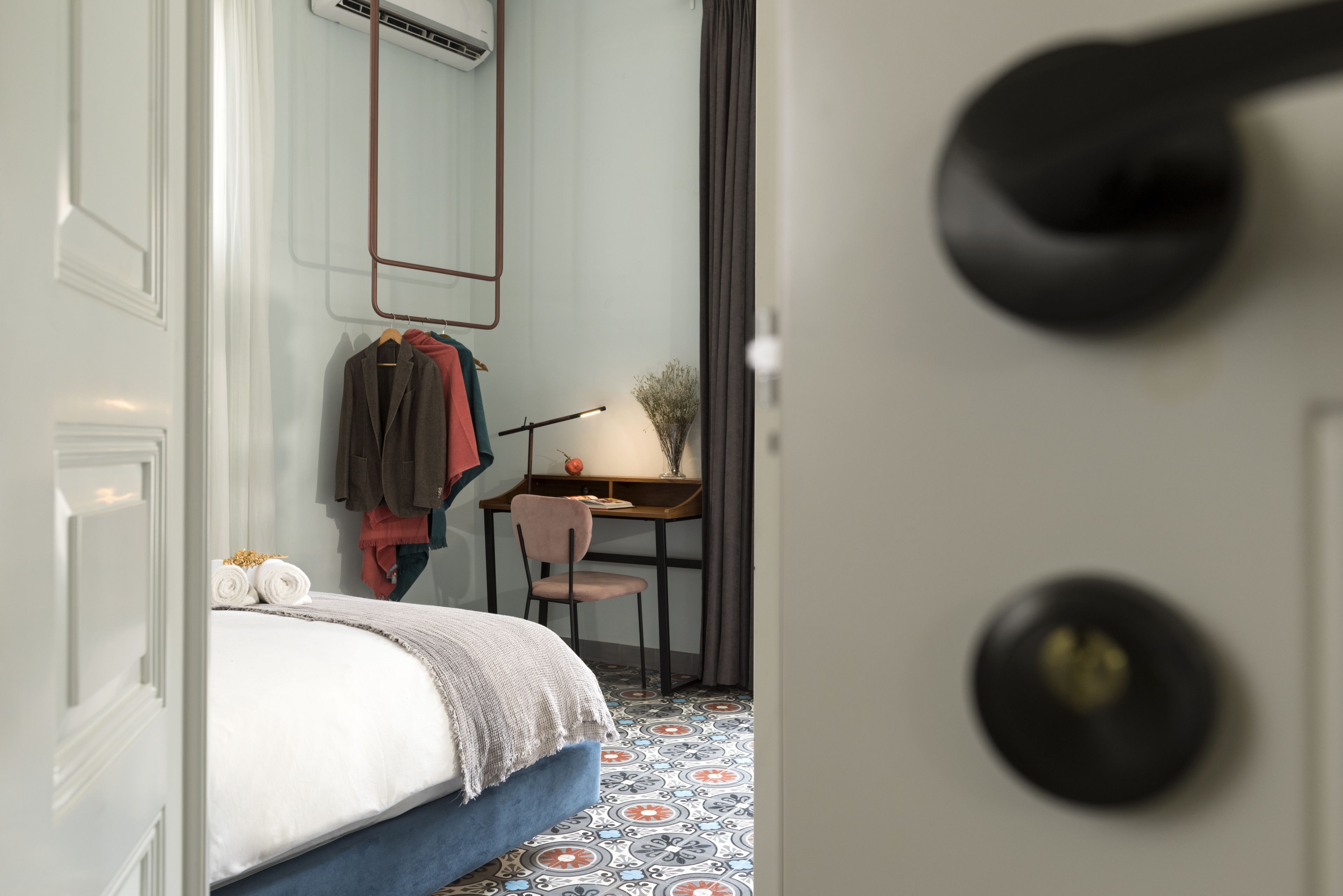 A hotel room with a bed, a desk, a chair, and a mirror.