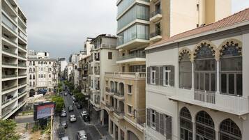 Une vue d’une rue de la ville, avec des immeubles à plusieurs étages, un ciel dégagé et des voitures sur la chaussée.