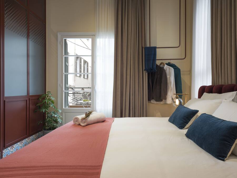 Habitación de hotel con una cama grande, una ventana con cortinas, una planta en maceta y vistas al balcón exterior.