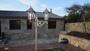 A stone building with a tiled roof, a wrought iron lamp post, and a stone wall with a planter.