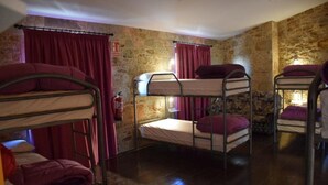 A room with bunk beds, stone walls, and red curtains.