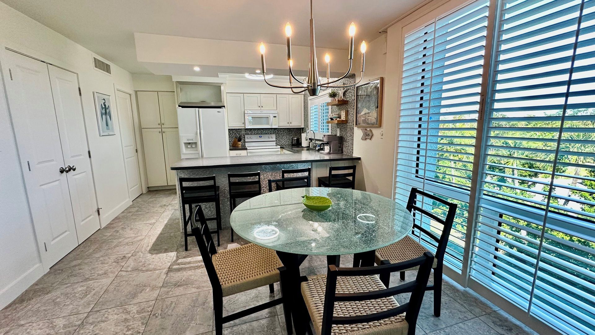 A modern kitchen with a round glass table, black chairs, and a chandelier.