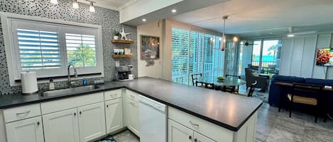 A modern kitchen with a central island, a dining area with a view, and a living space with a TV.
