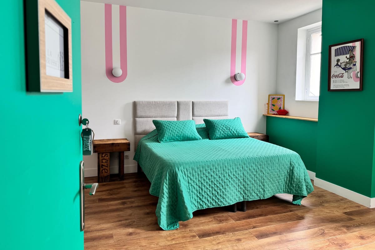 A bedroom with a bed, a nightstand, a wall-mounted light, and a window.