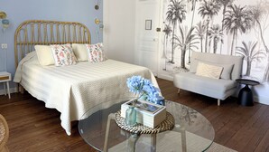 Un dormitorio con cama, sofá, una mesa de centro de vidrio y una pared con un mural tropical.