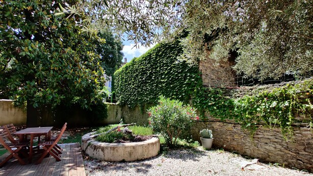Un jardín con terraza de madera, una maceta circular y un muro de piedra.
