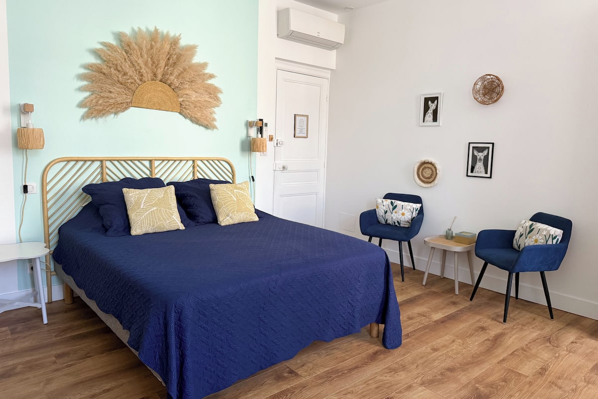 A bedroom with a bed, two chairs, a small table, and a wall-mounted decorative piece.