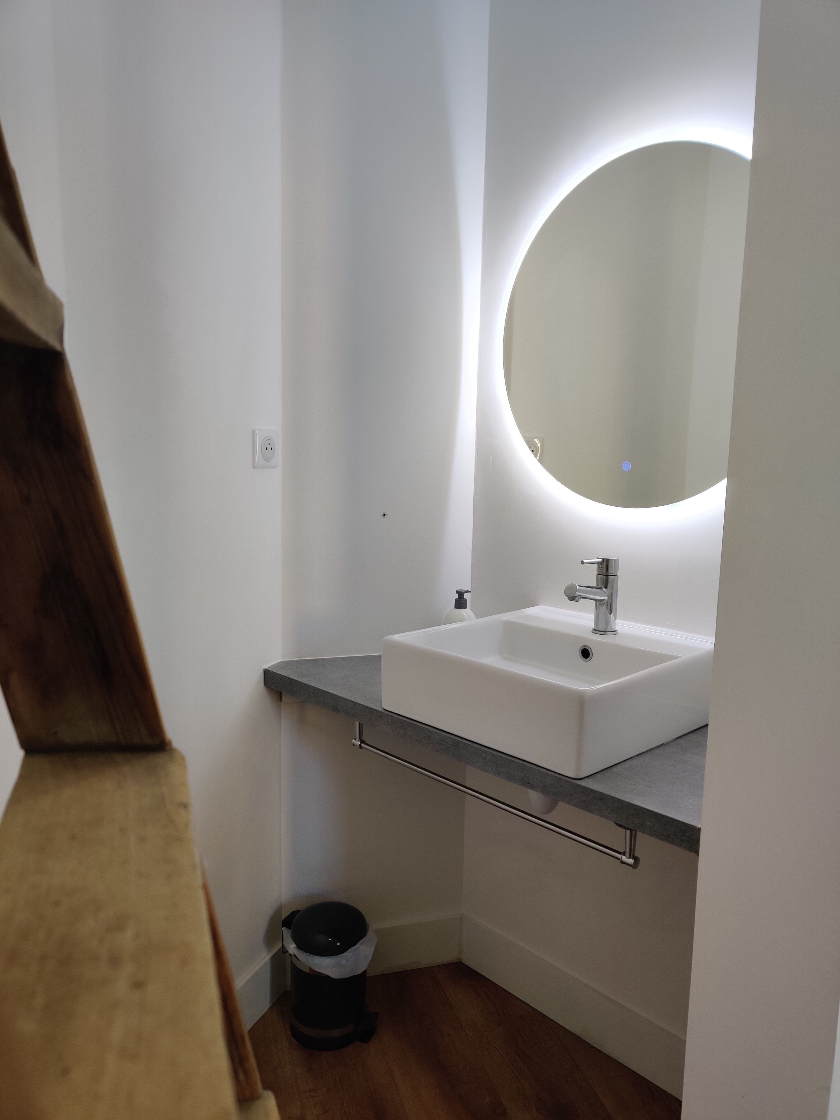 Un baño con un lavabo blanco, un espejo redondo y un cubo de basura.