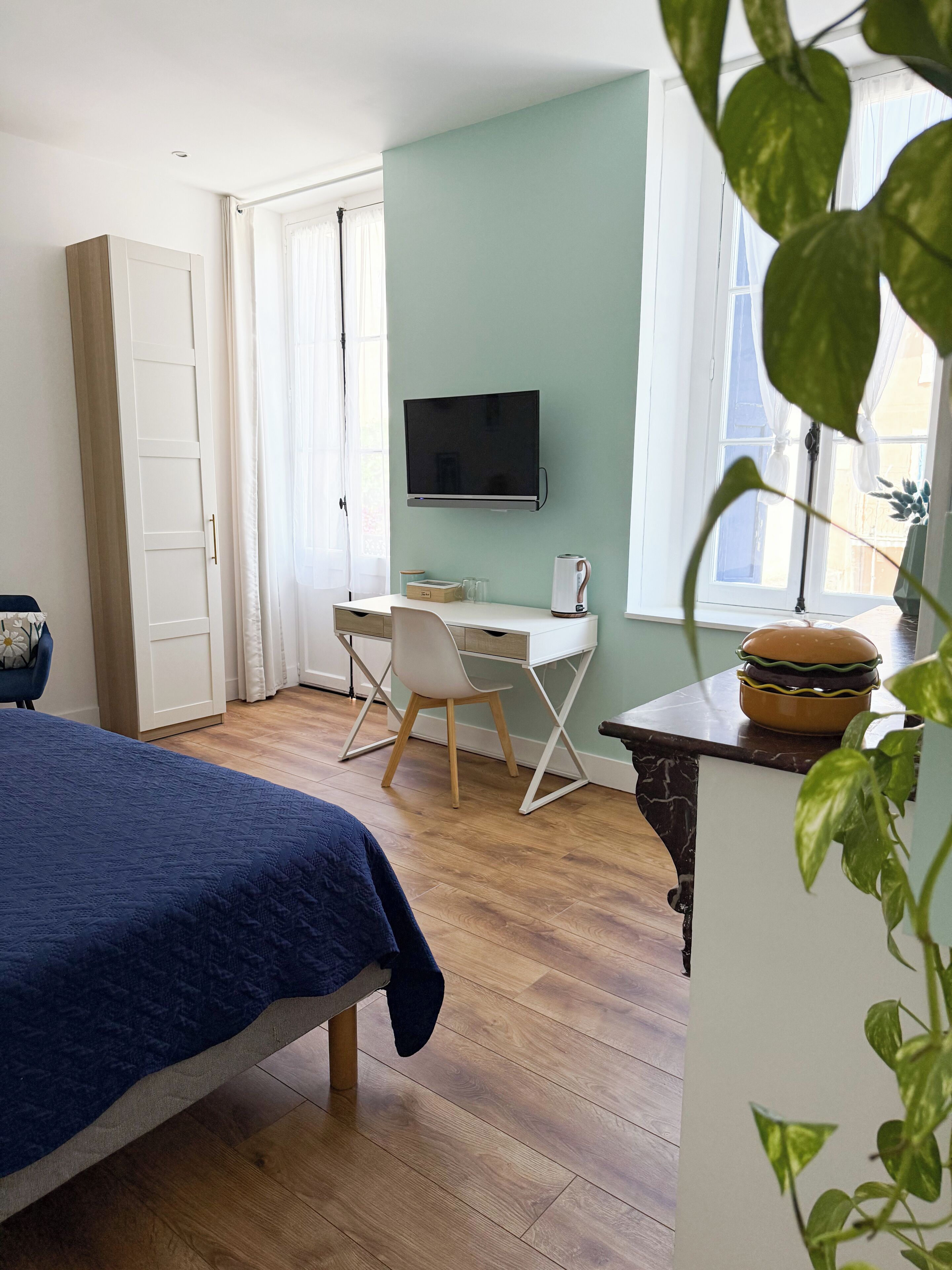 A bedroom with a bed, a desk, a chair, a television, and a window.
