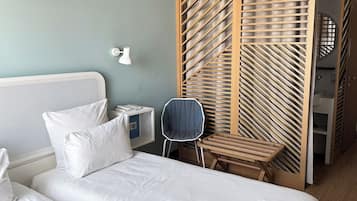 Habitación de hotel con cama, silla, mesita de noche, lámpara de pared y panel divisor de madera.