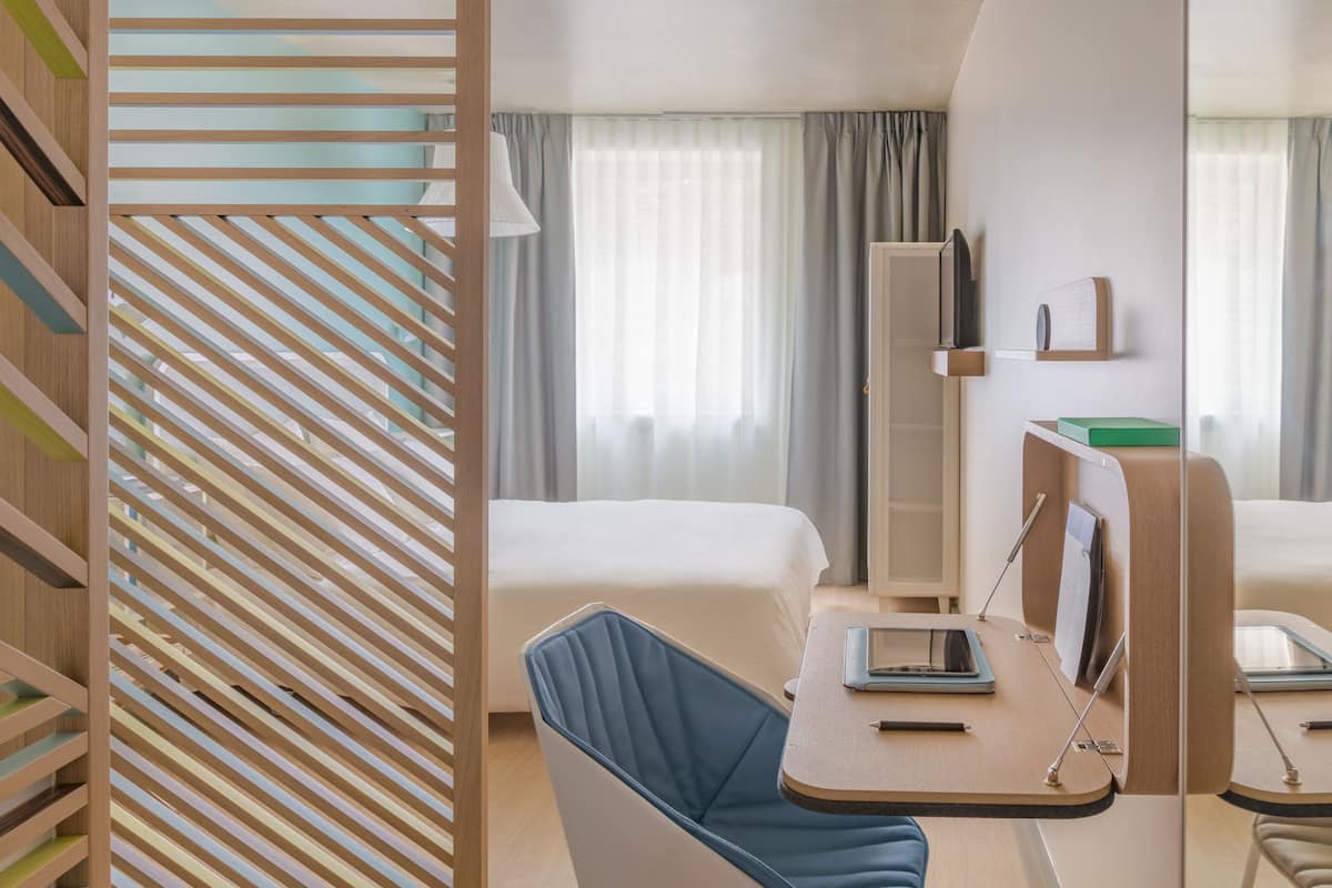 Una habitación de hotel con cama, escritorio, silla, espejo y televisor.