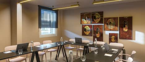 Un salón de conferencias con una larga mesa, sillas, computadoras portátiles y obras de arte en las paredes.