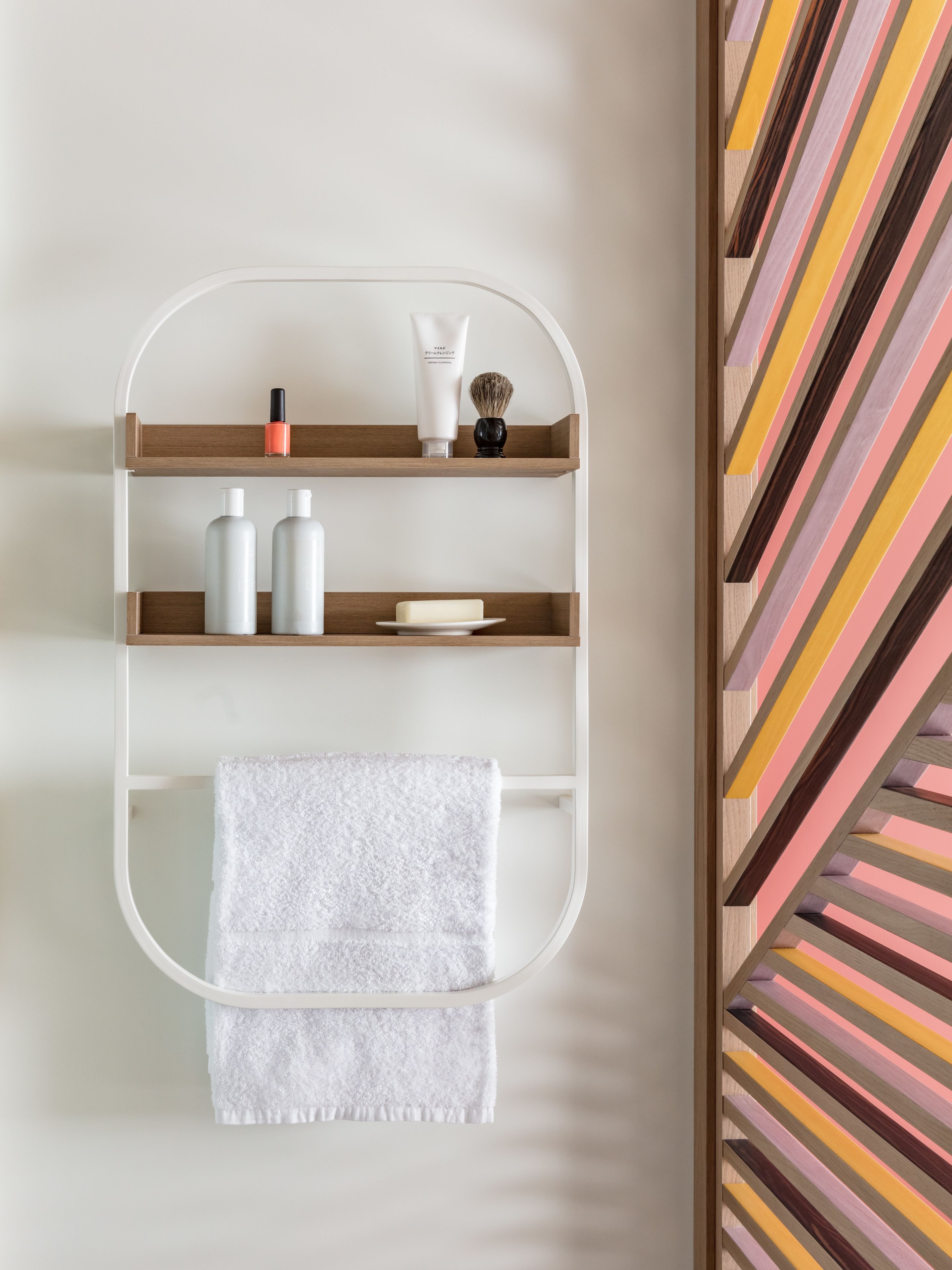 A bathroom with a white towel hanging on a rack, a shelf with toiletries, and a striped wall pattern.