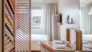 Ein modernes Hotelzimmer mit großem Fenster, Schreibtisch mit Stuhl, Bett und dekorativer Holzwand.