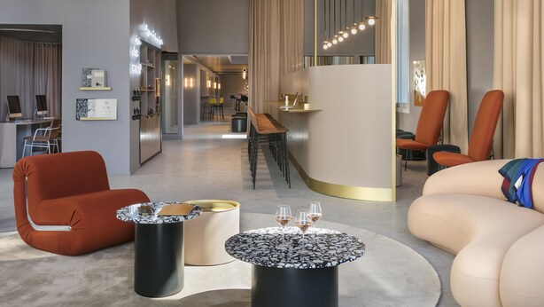 Ein modernes Interieur mit einer Couch, Sesseln, einem runden Tisch mit Gläsern, einer Küchenzeile und einer Treppe.