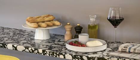 A dining table with a marble top, a white cake stand with pastries, a glass of red wine, and a bottle of olive oil.