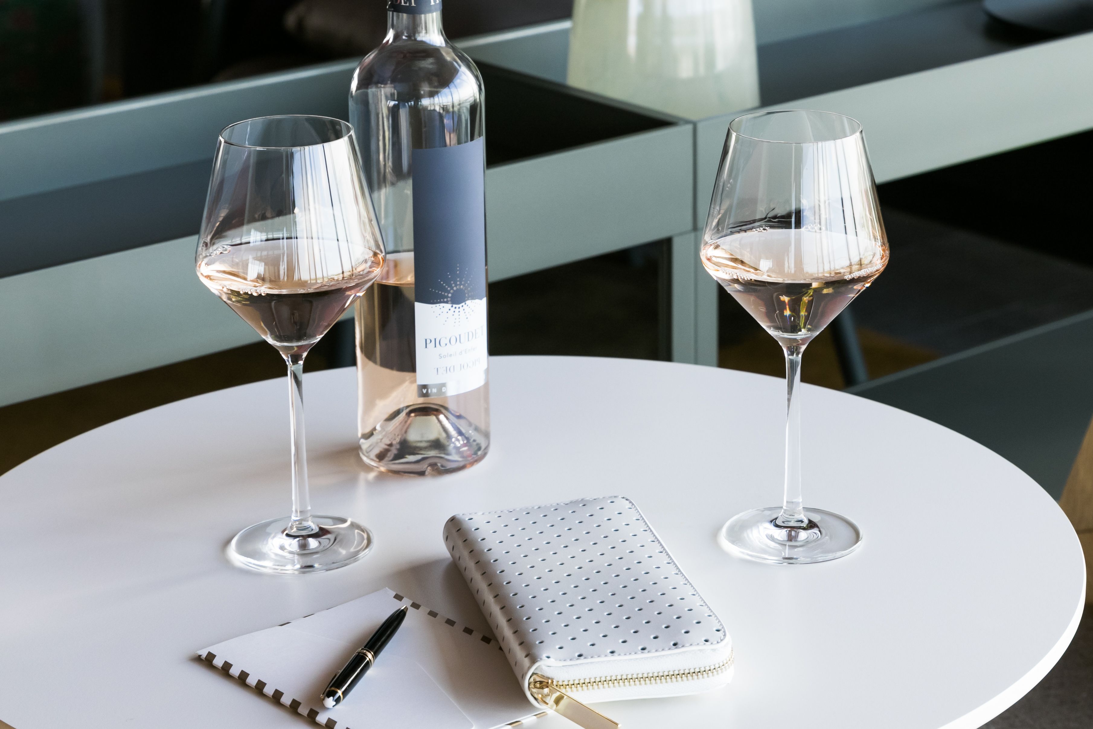 A round white table with two wine glasses, a bottle of wine, a notebook, and a pen.