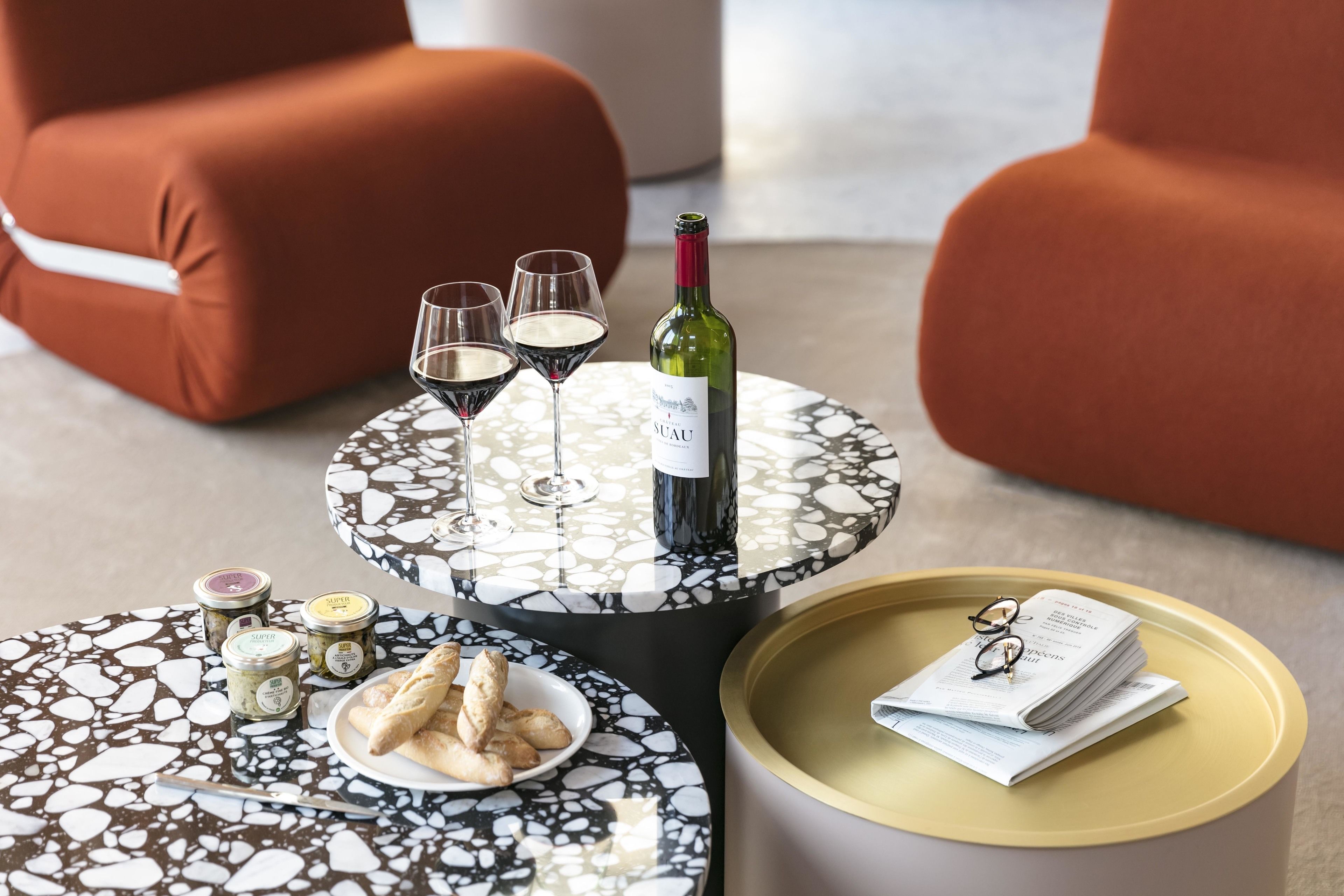 A round table with a marble pattern, a bottle of wine, two wine glasses, a plate with pastries, and a tray with glasses and a book.