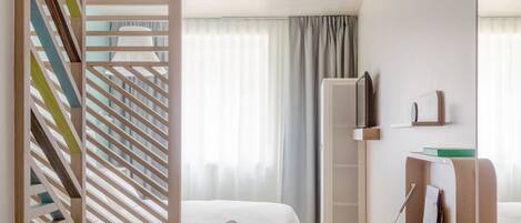 Una habitación de hotel moderna con cama, escritorio con silla, estantería y un separador decorativo de madera.