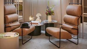 Ein moderner Lounge-Bereich mit Ledersesseln, einem runden Tisch mit Blumenvase und einer Neonleuchtreklame an der Wand.
