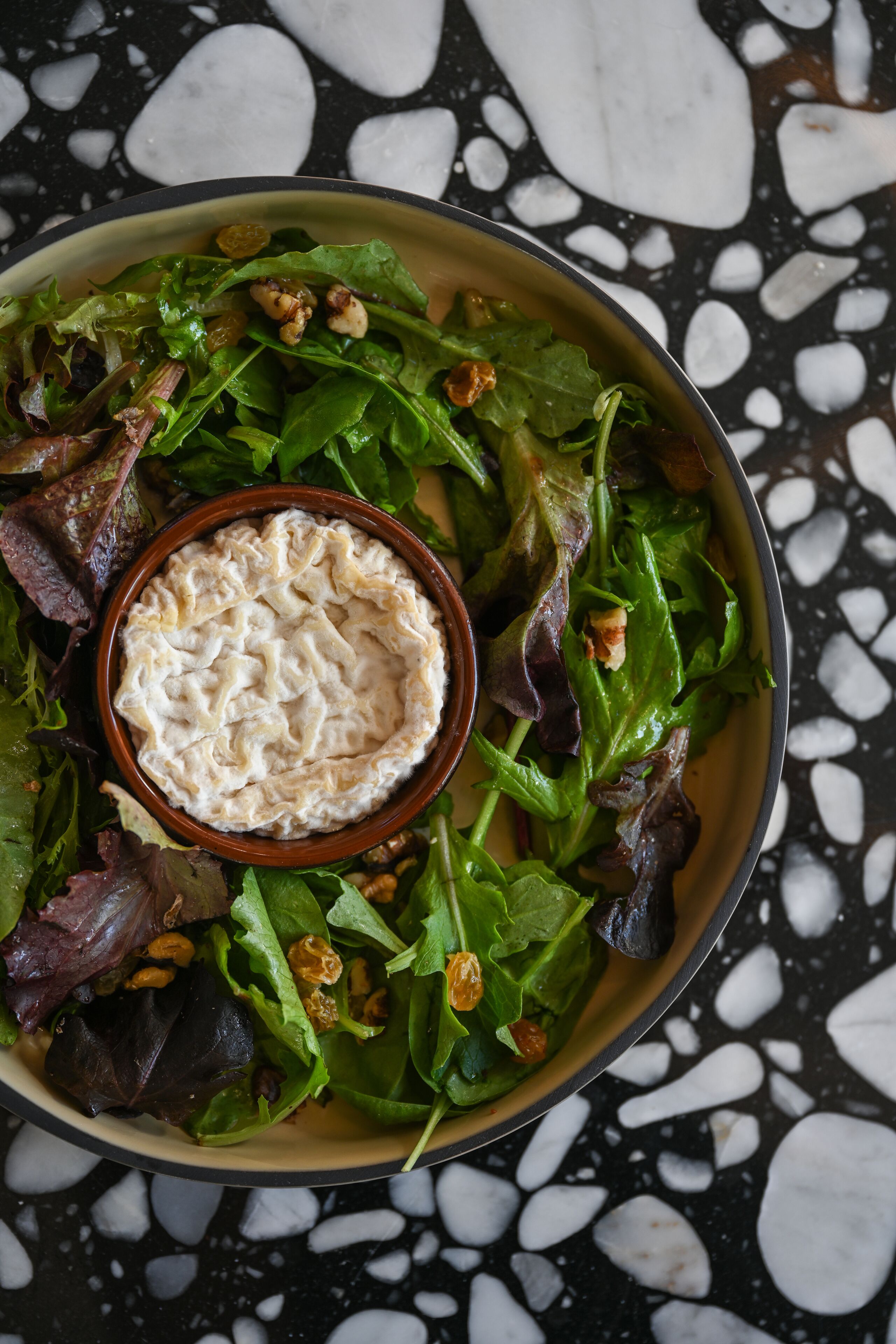 A bowl of salad with a creamy dip on a black and white speckled surface.