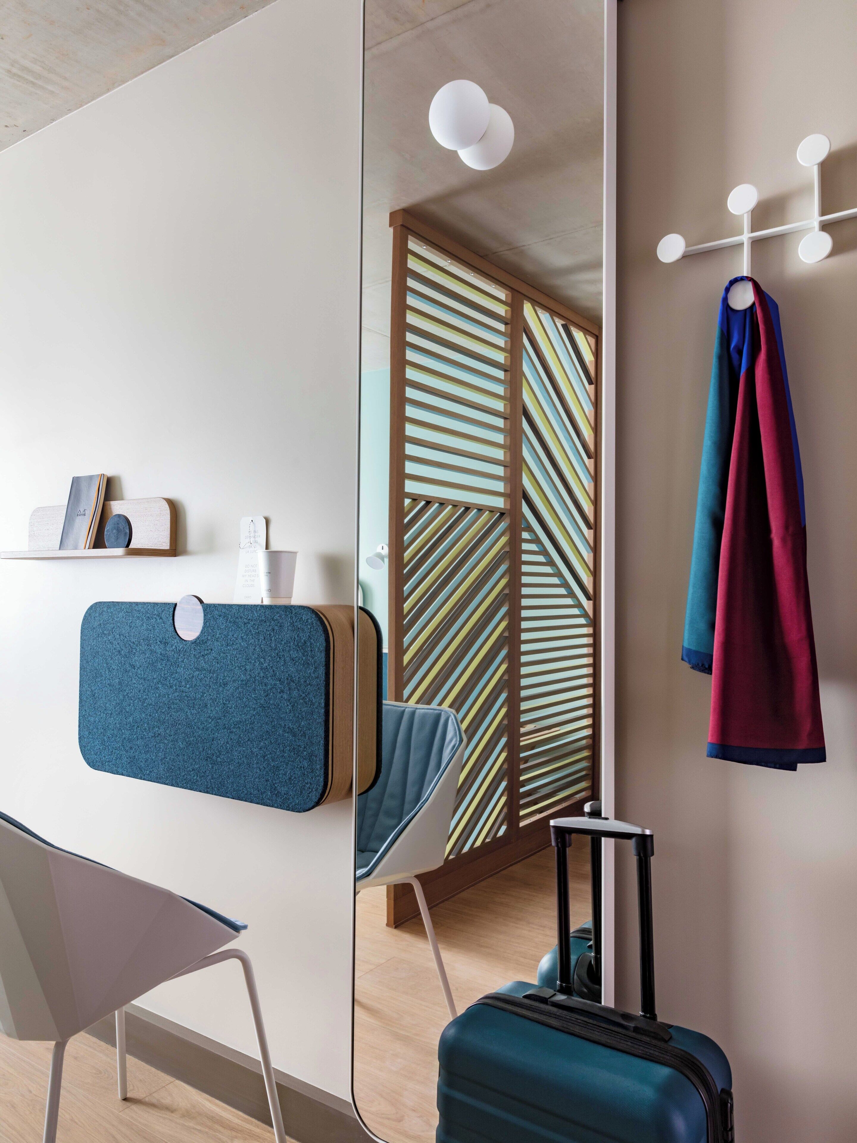 Habitació d'hotel moderna amb escriptori, cadira, penjador fixat a la paret i paper tapet vistós.