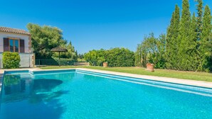 Une piscine d’un bleu éclatant, bordée de carreaux, entourée de verdure et donnant sur une maison dotée d’un balcon.