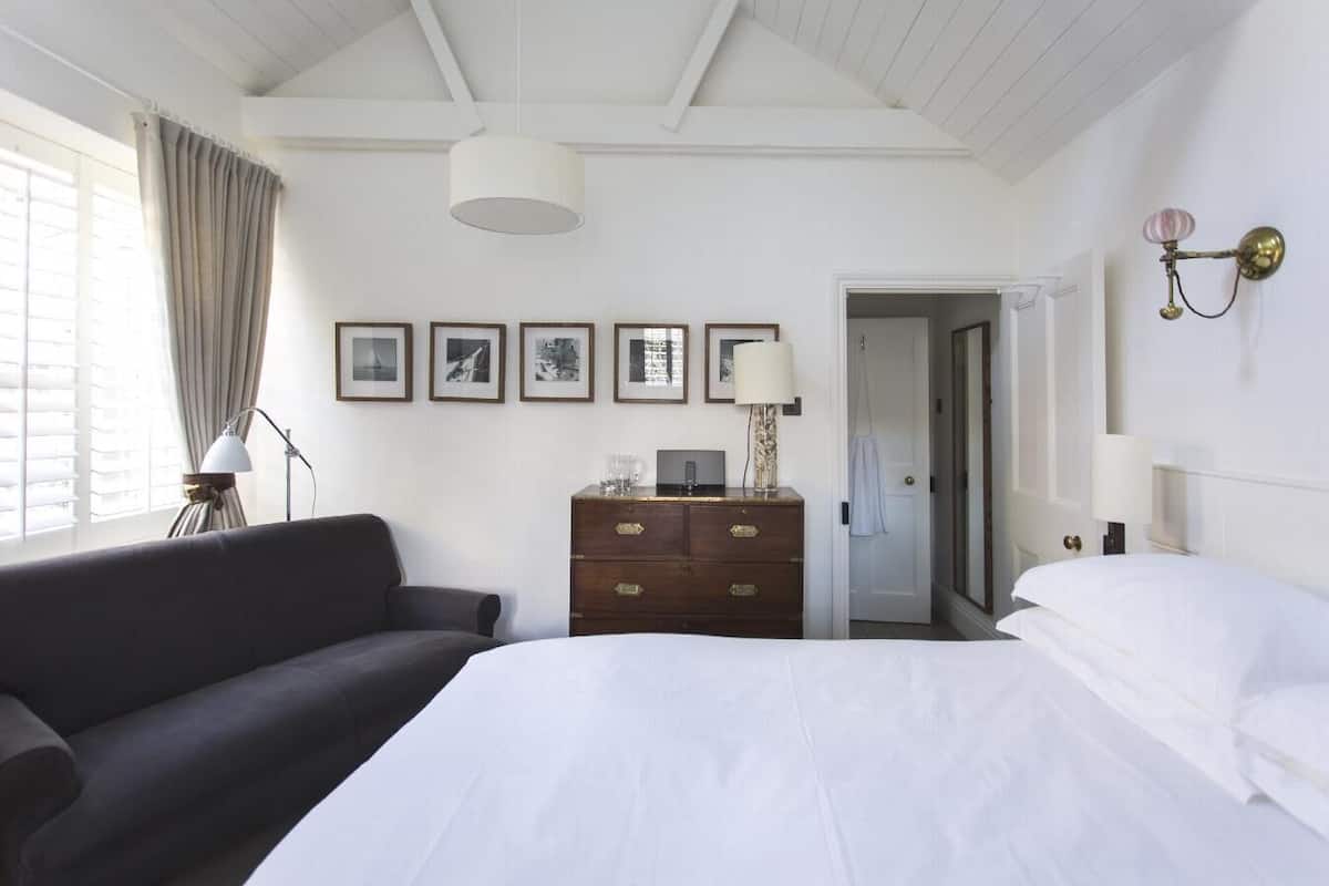 A hotel room with a large bed, a dark sofa, a wooden dresser, and framed pictures on the wall.