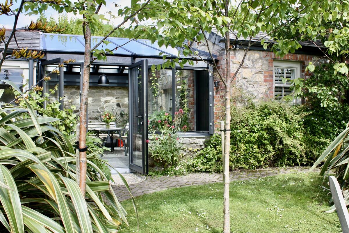 A conservatory with a glass door, a stone wall, and a garden with various plants and flowers.