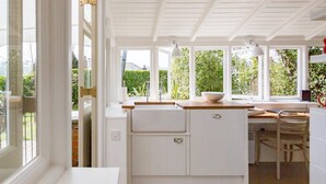 A bright kitchen with white cabinetry, a wooden countertop, and a view of greenery outside.