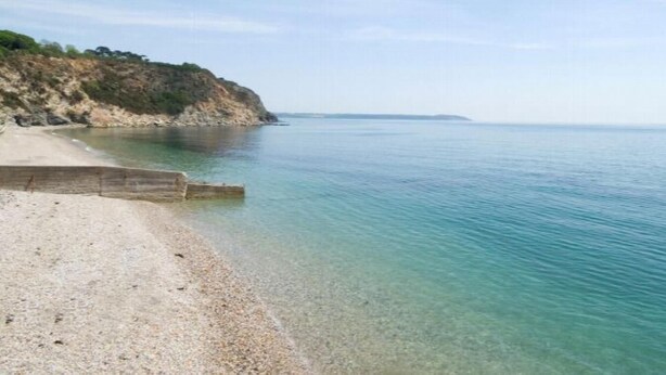 A beach with clear water, a sandy shore, and a rocky cliff.