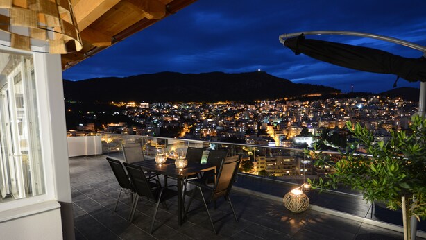 A rooftop terrace with a dining table and chairs, overlooking a cityscape at night. - "VERDE BLUE" – Stylish Loft with Panoramic Terrace in Kavala (Kavala)