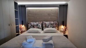 A modern hotel room with a large bed, two bedside tables with lamps, a wooden headboard, and a floral-patterned pillow. - "VERDE BLUE" – Stylish Loft with Panoramic Terrace in Kavala (Kavala)