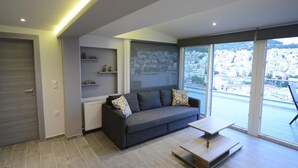 A modern living room with a grey sofa, a coffee table, and a city view through large windows. - "VERDE BLUE" – Stylish Loft with Panoramic Terrace in Kavala (Kavala)