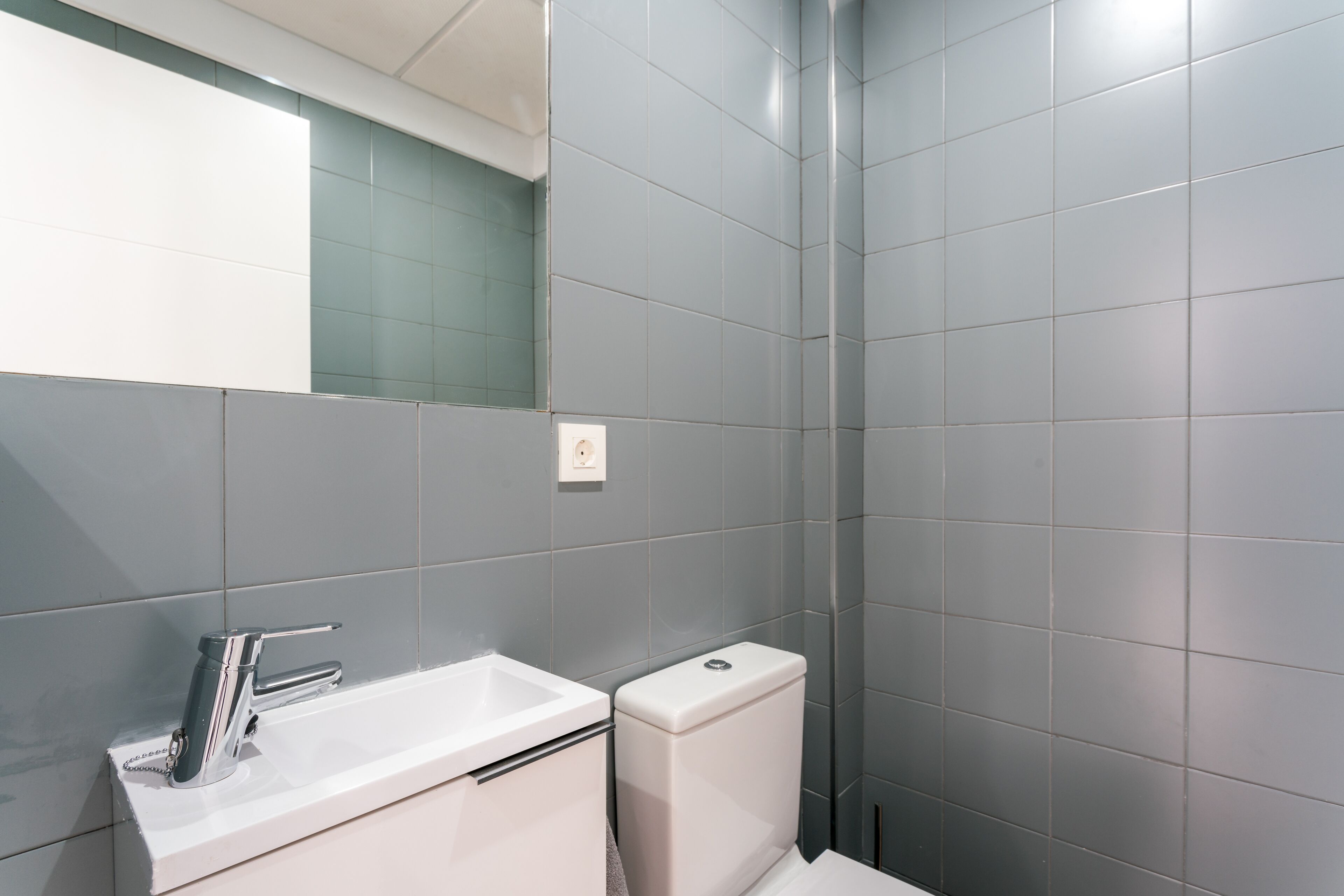 A modern bathroom with a white sink, chrome faucet, and a toilet.