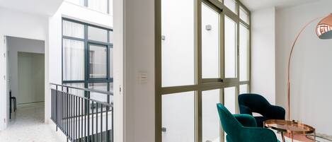 A modern interior with large windows, a balcony, and two teal chairs by a small table.