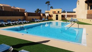 A rectangular swimming pool with clear blue water, surrounded by a low fence and several lounge chairs.